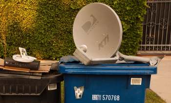 A DirecTV satellite dish and a cable box sit on top of a blue trash can, alongside a remote control.