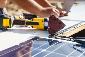 Tools and a solar panel are visible on a work surface, with hands working on modifications.