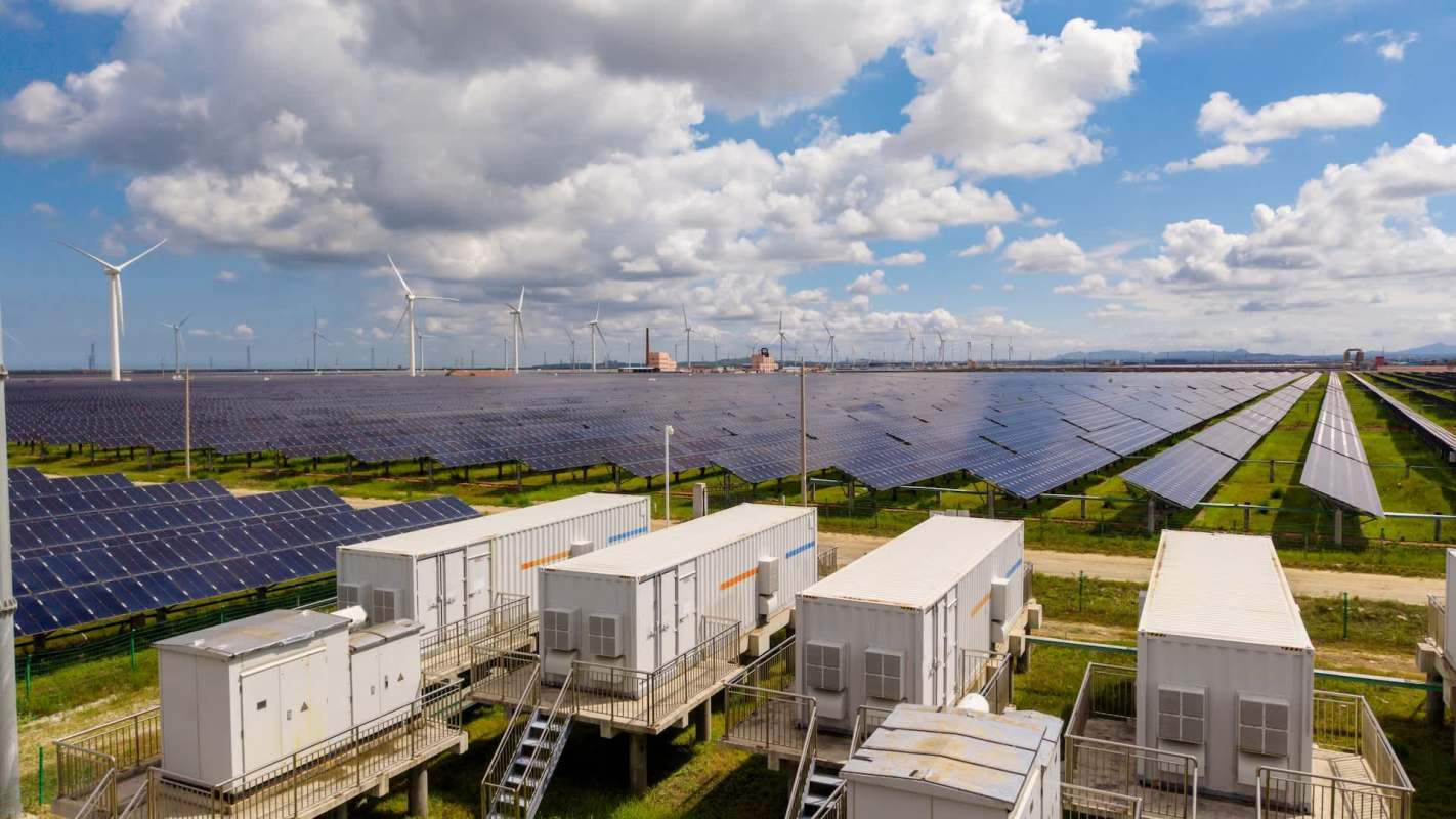 A solar farm with multiple solar panels and wind turbines under a partly cloudy sky.
