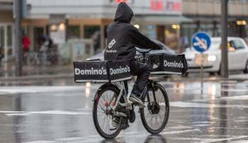 A delivery person on a bicycle rides through rain, carrying Domino's pizza boxes.