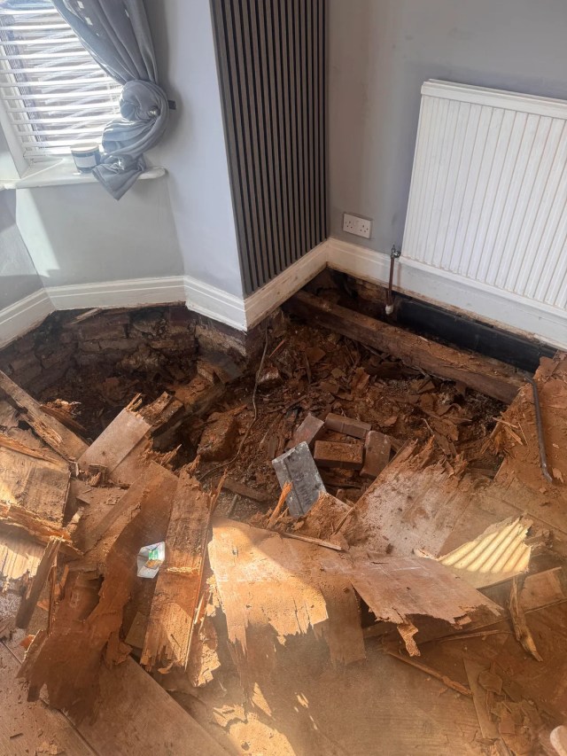 A room under renovation with exposed flooring, scattered debris, and a partially removed section of the floor.