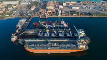 Aerial view of multiple cargo ships docked at a port with cranes and industrial buildings in the background.