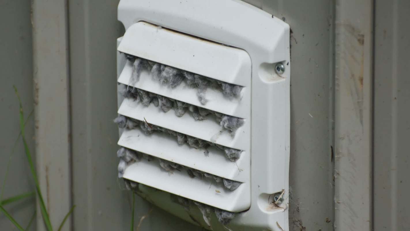 A vent covered in dust and lint, mounted on a gray wall.