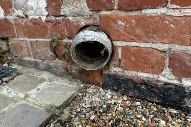 A dryer vent sticking out of a brick wall.