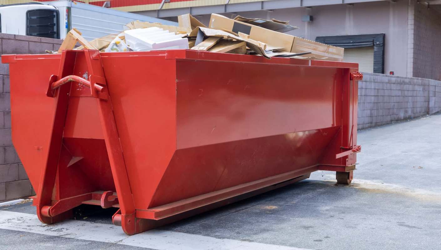 A red dumpster filled with various items is parked next to a building.