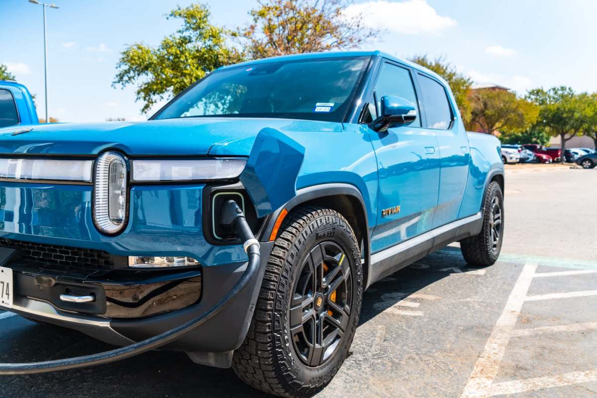 An electric blue truck with a charging cable plugged in, parked in a parking lot.