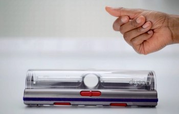 A hand gestures toward a Dyson vacuum attachment on a flat surface.