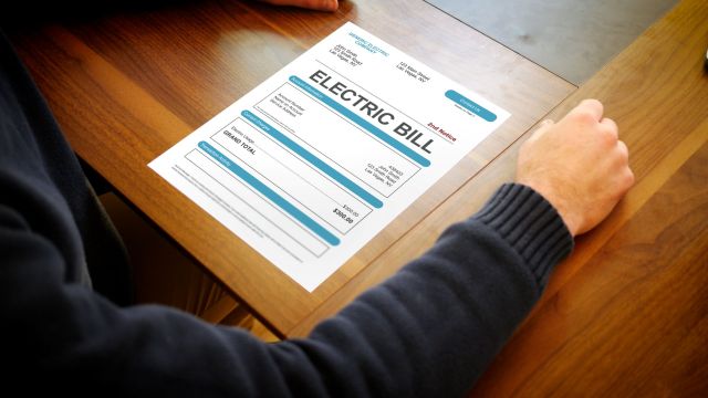 A person's hand rests on a table next to an electric bill document.