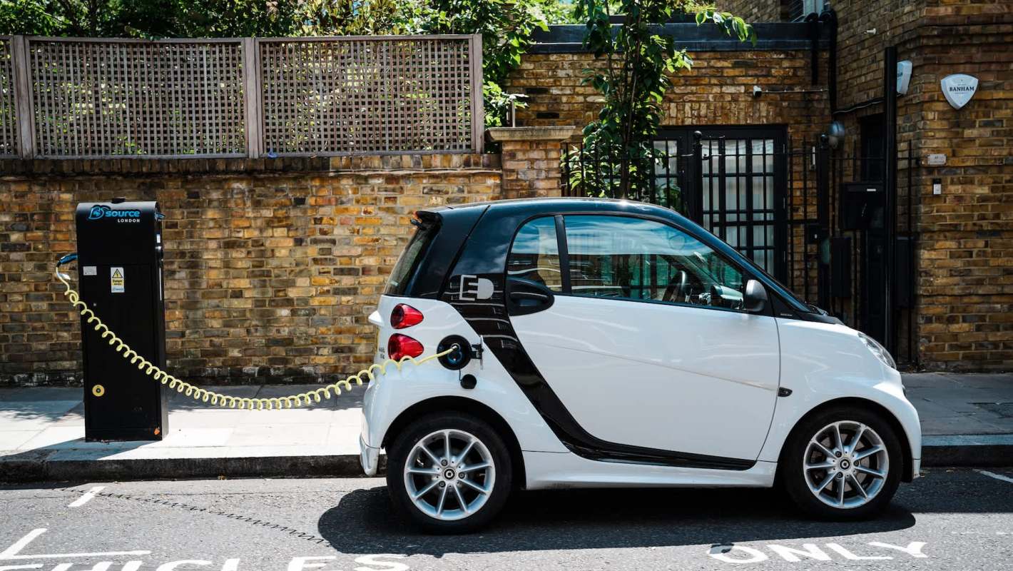 A small electric car charging at a station on a city street.
