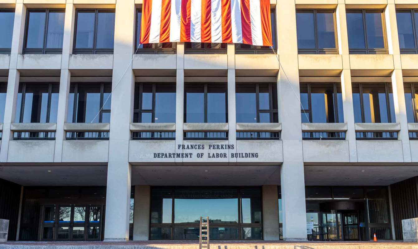 The entrance of the Frances Perkins Department of Labor Building with an American flag displayed above.