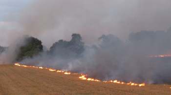 A field is burning with flames and smoke rising into the air.