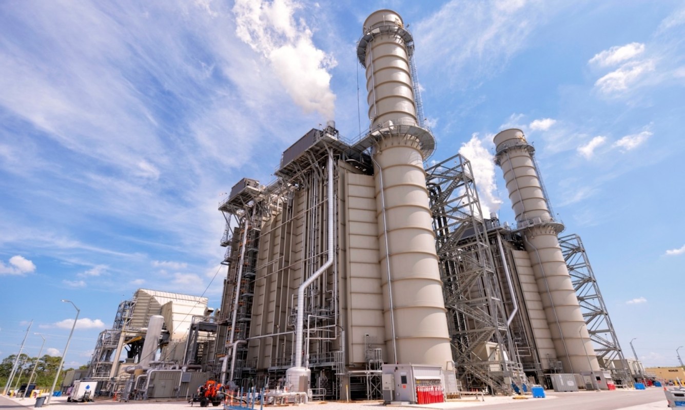 A large industrial power plant with tall smokestacks and complex machinery under a blue sky.