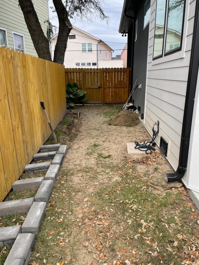 A dirt walkway between a house and a wood fence. 