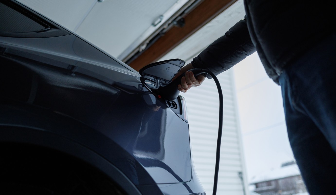 A person plugs an electric vehicle into a charger in a garage.