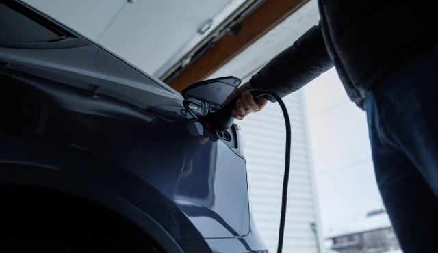 A person plugs an electric vehicle into a charger in a garage.