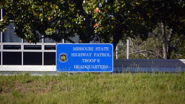 A sign for the Missouri State Highway Patrol Troop E Headquarters in front of a building and trees.