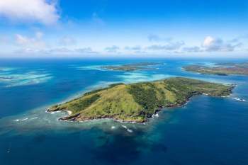 An aerial view of an island surrounded by turquoise waters and coral reefs.