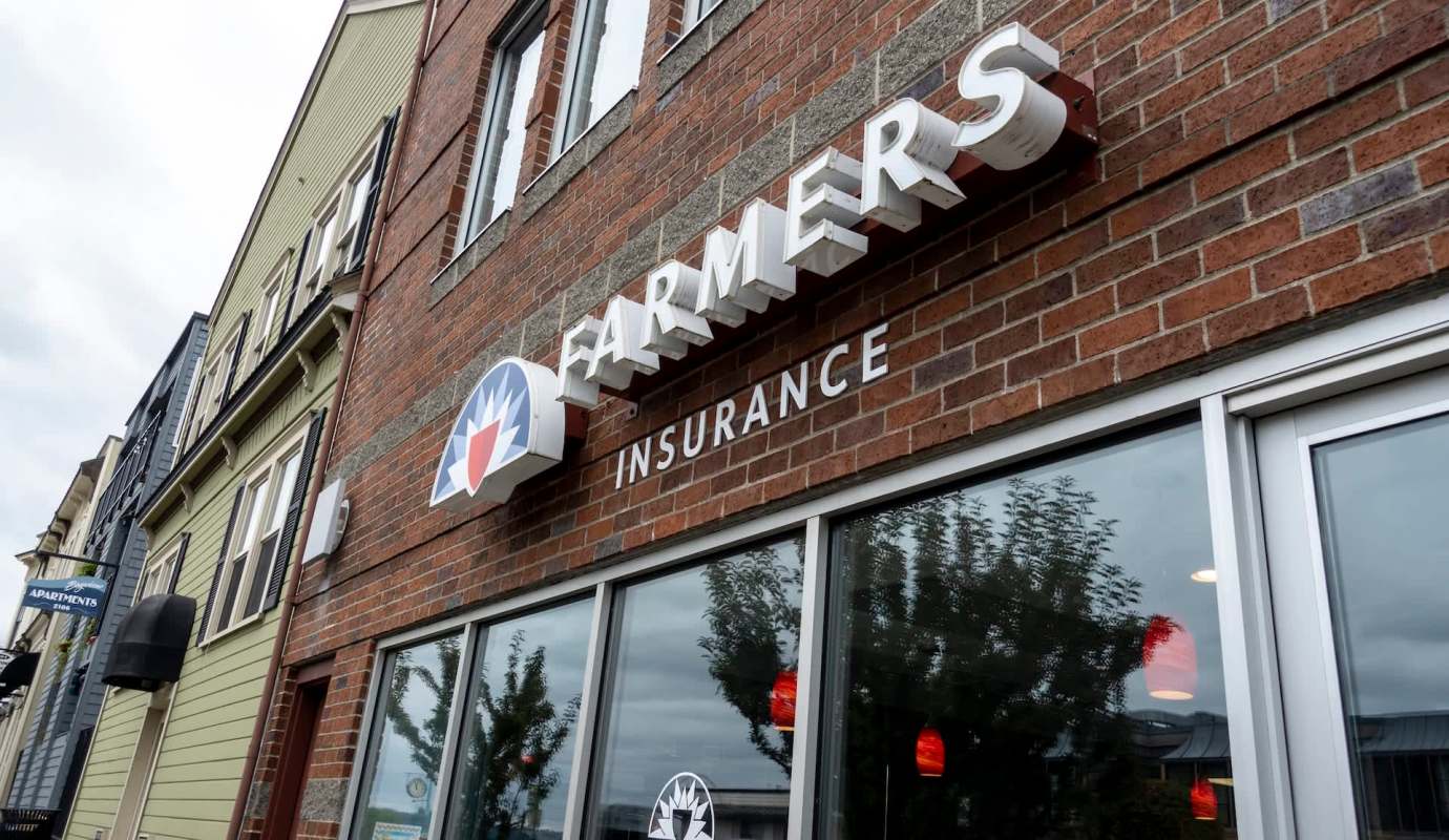 A brick building with a sign for Farmers Insurance and nearby apartment signs.
