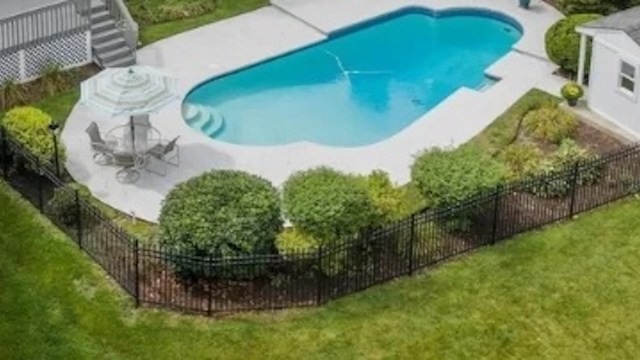 A backyard with a swimming pool, patio furniture, and a surrounding fence.