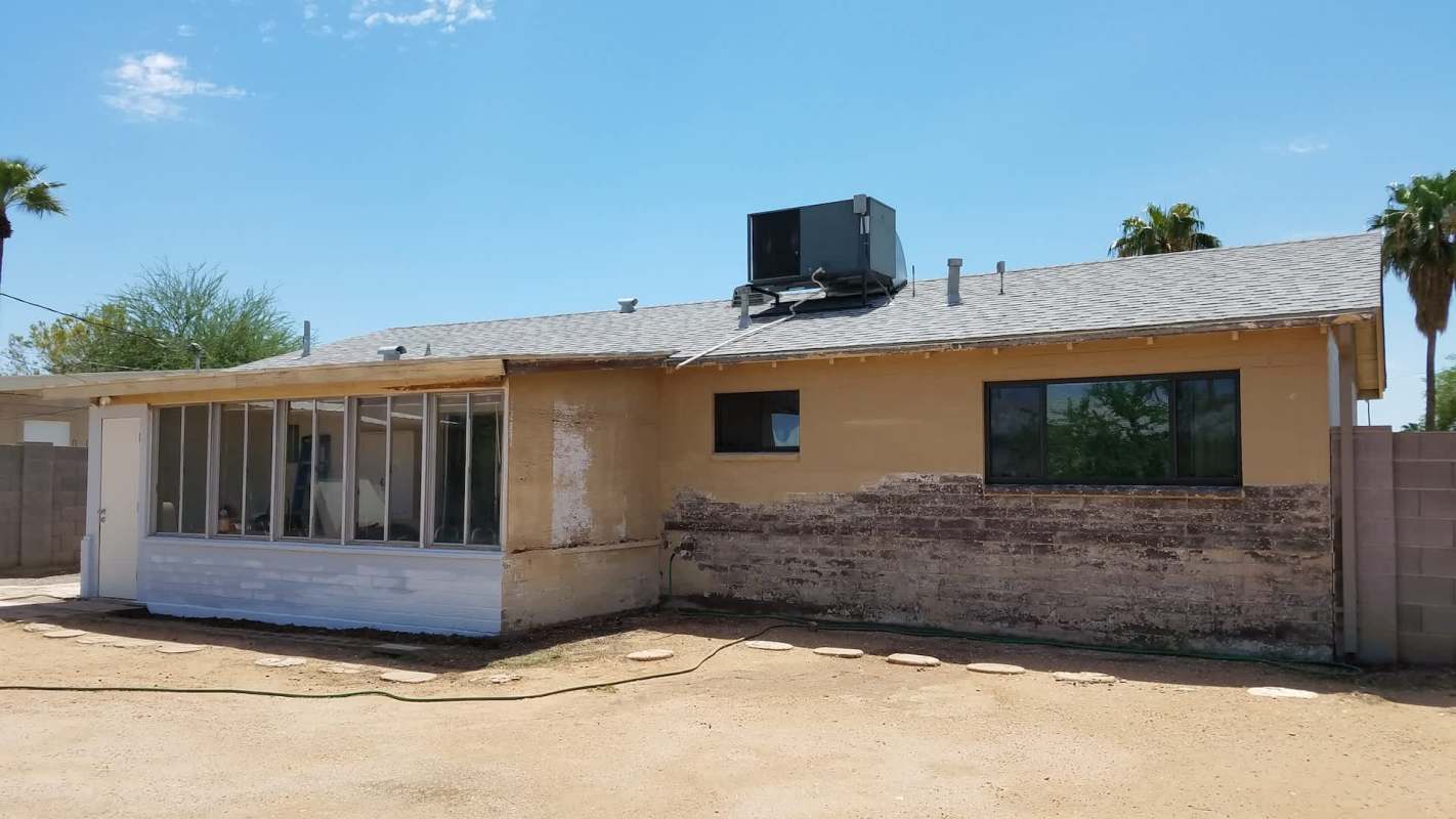 A partially renovated single-story house with a missing paint section and an air conditioning unit on the roof.