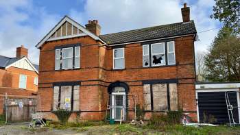 An abandoned two-story brick house with boarded windows and a shopping cart in the overgrown yard.