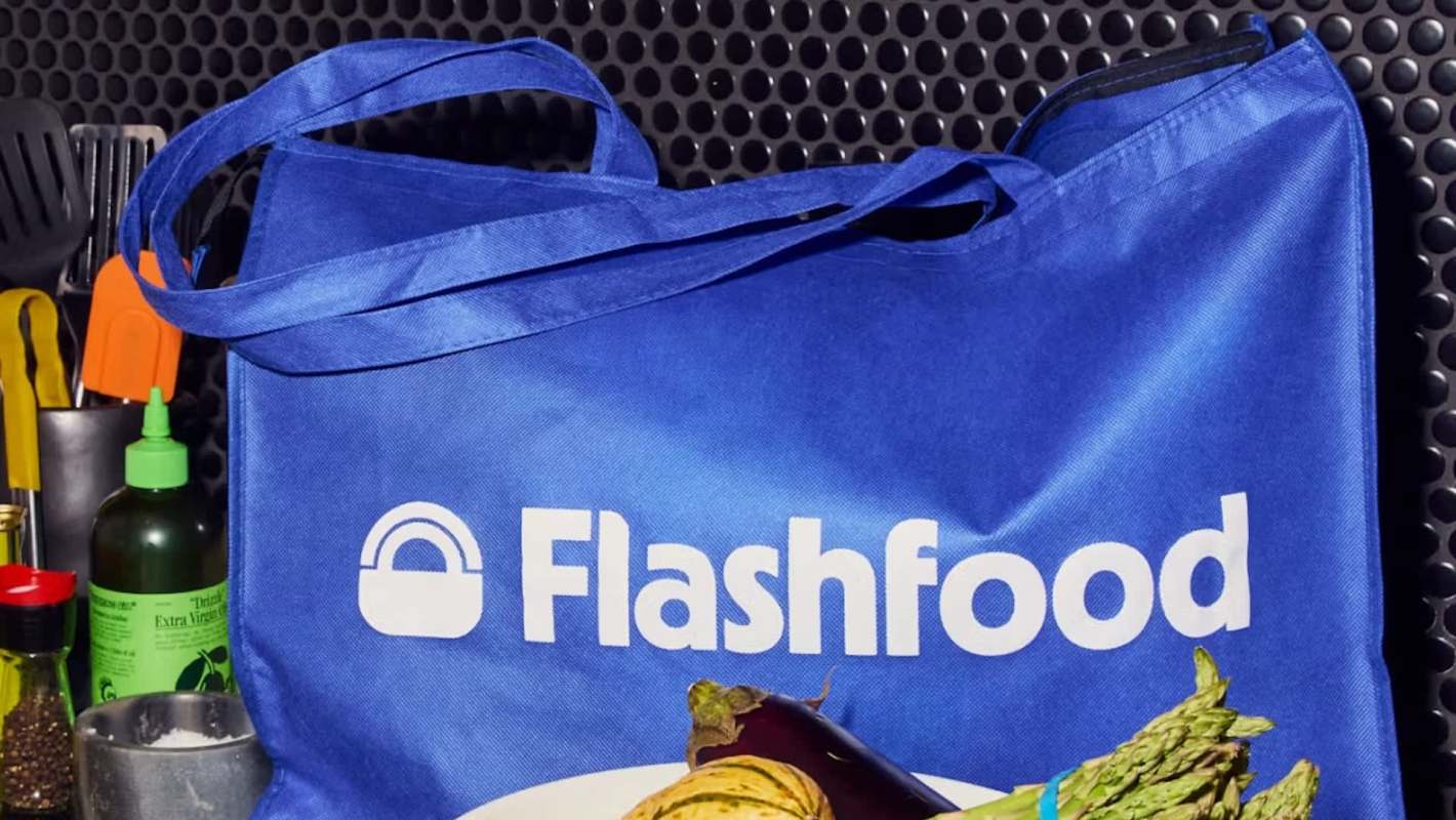 A blue reusable bag with the logo "Flashfood" and assorted vegetables in front of it.