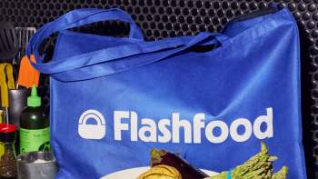 A blue reusable bag with the logo "Flashfood" and assorted vegetables in front of it.