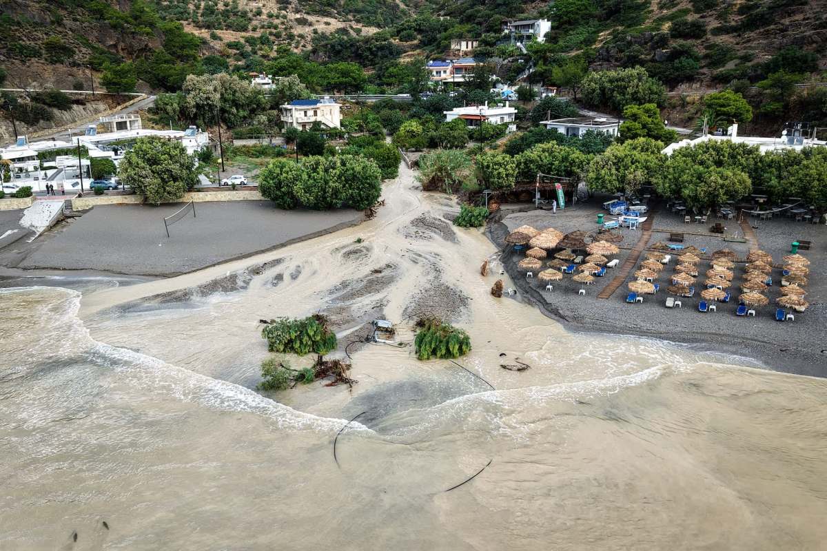 A beach area affected by flooding, with sandy ground and scattered umbrellas.