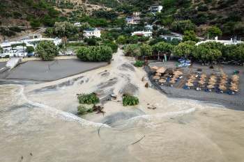 A beach area affected by flooding, with sandy ground and scattered umbrellas.