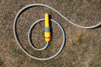 A garden hose with a yellow nozzle lying on dry grass.