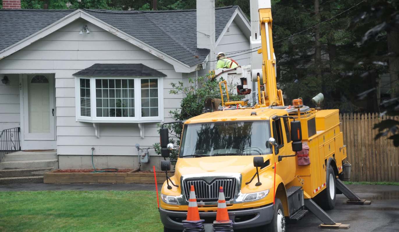 A utility truck with equipment parked in front of a house while a worker is on the roof.