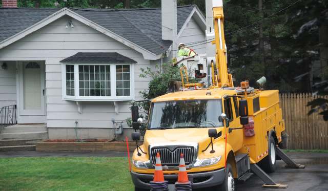 A utility truck with equipment parked in front of a house while a worker is on the roof.