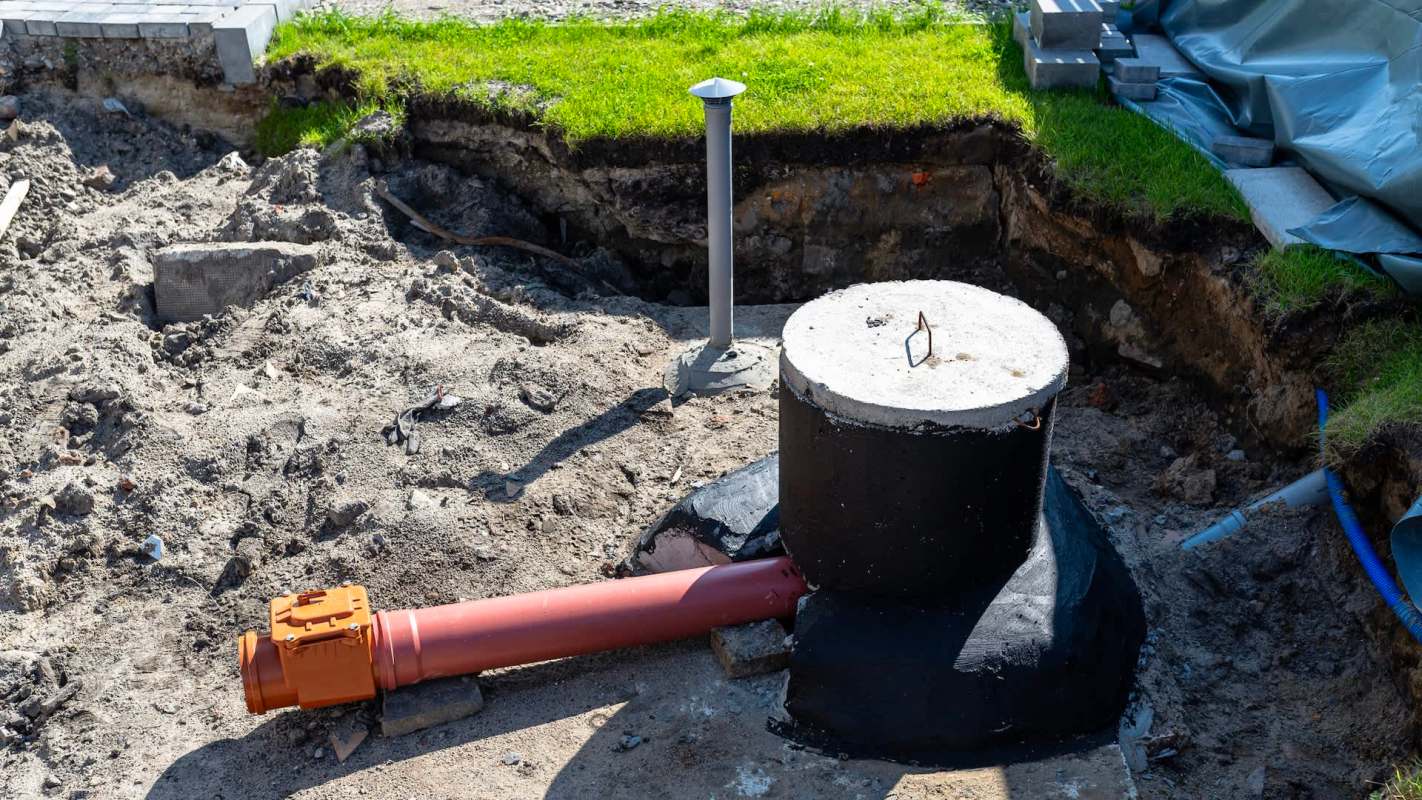 A construction site with an exposed drainage system and a large black pipe connected to a concrete fixture.