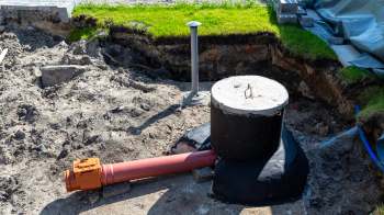 A construction site with an exposed drainage system and a large black pipe connected to a concrete fixture.