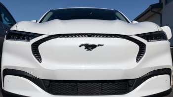 A white Ford Mustang Mach-E with a prominent logo on the front grille.