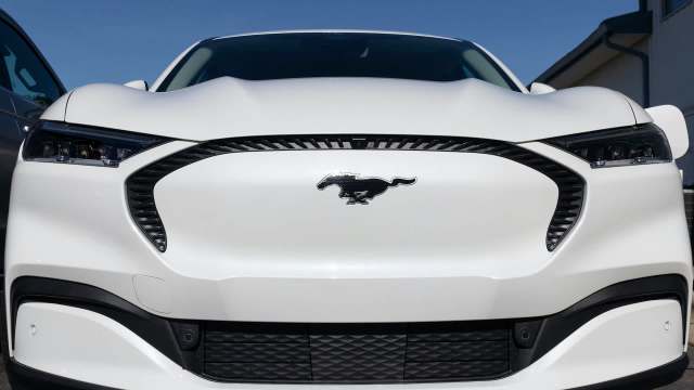 A white Ford Mustang Mach-E with a prominent logo on the front grille.
