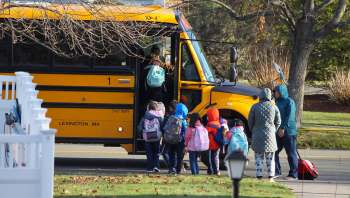 A group of children boards a school bus while a parent waits nearby.