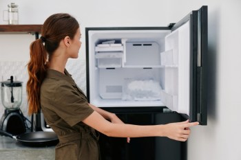 A woman looking in an empty freezer.