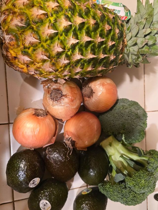 A pineapple, onions, avocados, and broccoli.