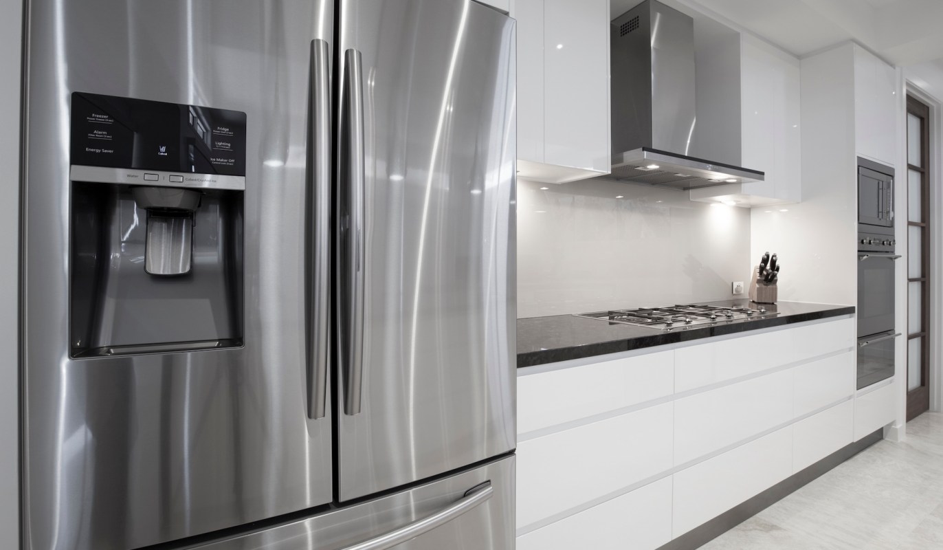 A modern kitchen featuring a stainless steel refrigerator, a gas stove, and white cabinetry.
