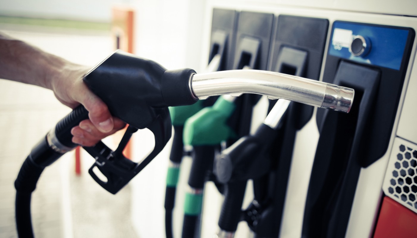 A hand holds a fuel pump at a gas station with multiple nozzles.