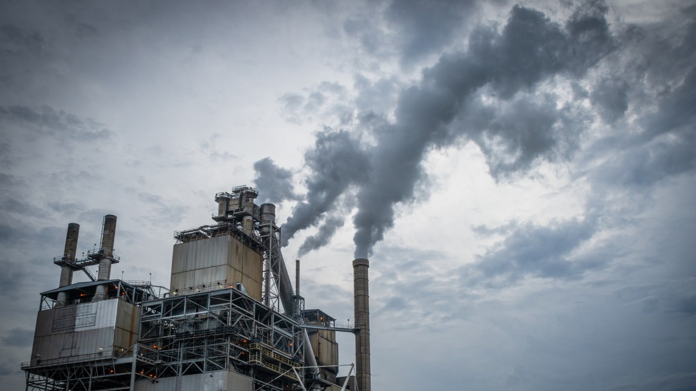 A factory releasing smoke into a cloudy sky.