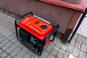 A red generator placed on a paved surface next to a wall.