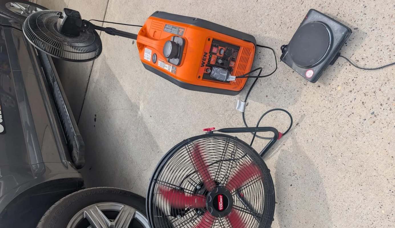 A power generator and a fan are set up on a concrete surface next to a vehicle.
