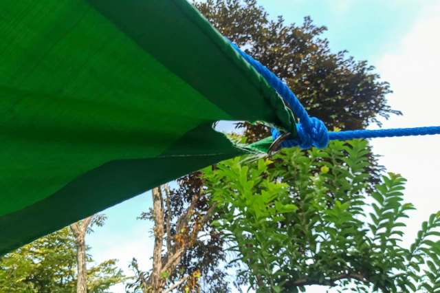 A green tarp secured with a blue rope amidst trees and a blue sky.