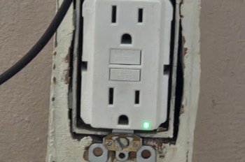 A electrical outlet with a green indicator light and exposed wiring.