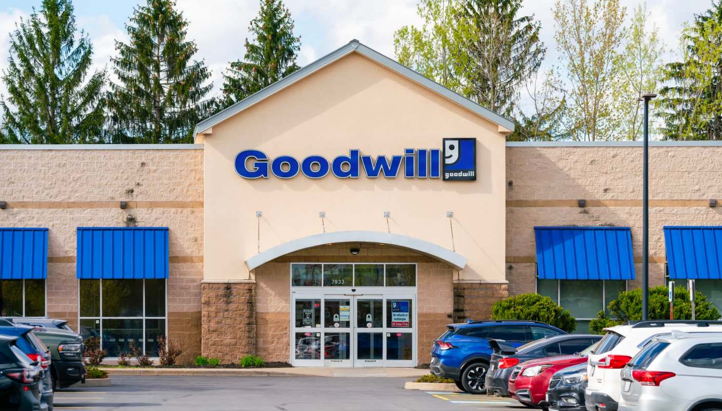 A Goodwill store with a blue awning and a parking lot filled with cars.