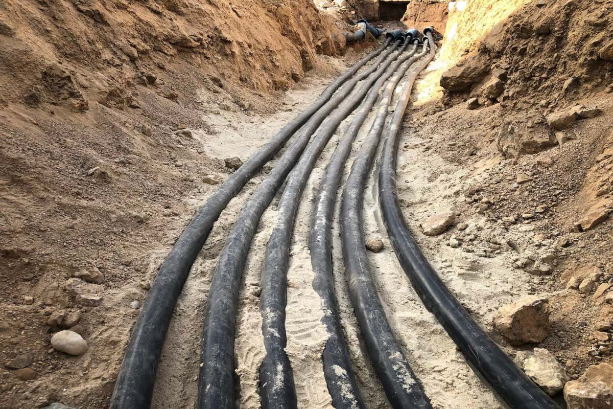 Several black cables run through a sandy trench surrounded by dirt and gravel.