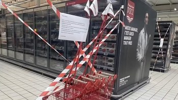 A section of a grocery store is closed off with caution tape and a sign, with shopping carts nearby.