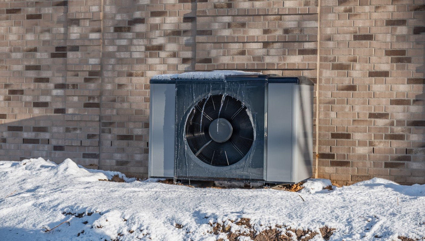 An outdoor air conditioning unit covered in ice and snow next to a brick wall.